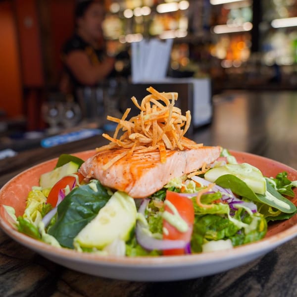 Grilled salmon salad with mixed greens, tomatoes, cucumbers, and crispy tortilla strips at Azteca D'Oro.