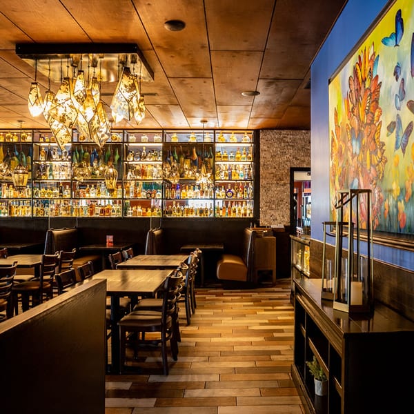 Interior of Azteca D'Oro Mexican Restaurant with tables, booths, a large tequila display, and butterfly artwork.