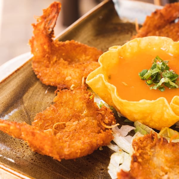Crispy fried shrimp and a tortilla bowl filled with orange sauce and cilantro on a brown plate.