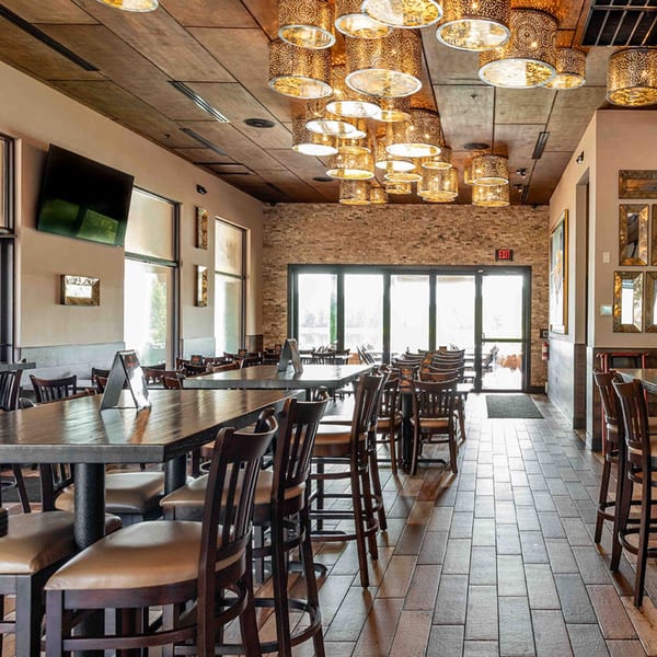 Interior of Azteca D'Oro Mexican Restaurant with high-top tables, chairs, and ornate golden light fixtures.