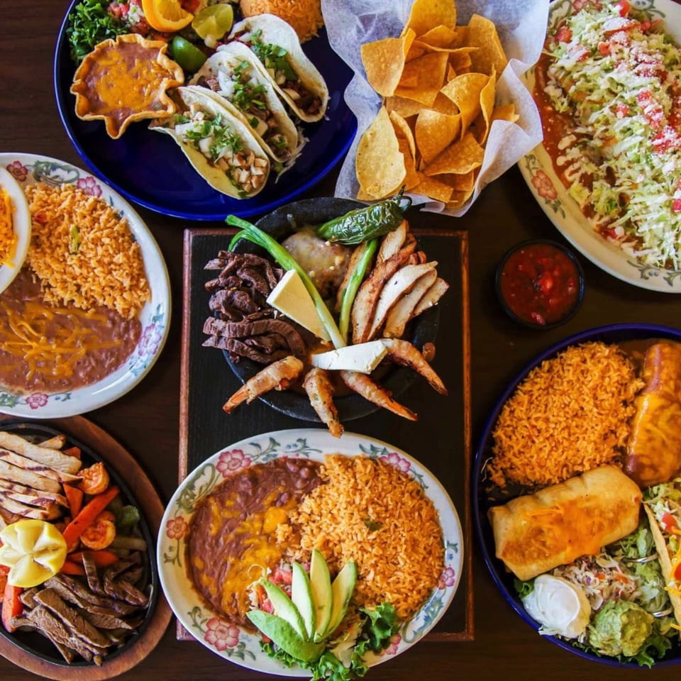 A vibrant spread of Azteca D'Oro Mexican dishes, including tacos, fajitas, rice, beans, and chips.