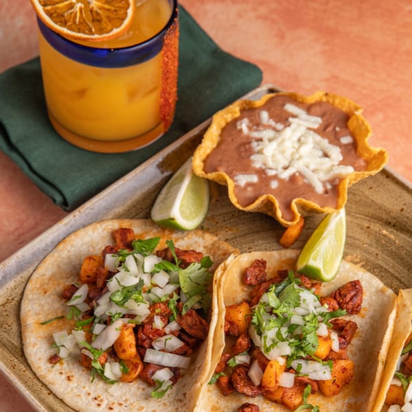 Three Azteca D'Oro al pastor tacos with lime, refried beans, and an orange margarita.
