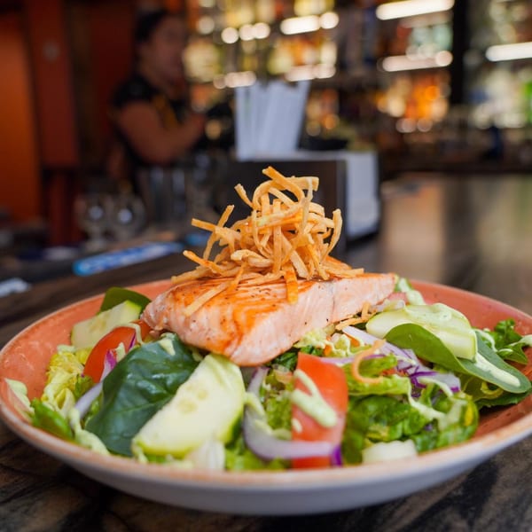 Grilled salmon fillet with crispy tortilla strips on a fresh salad with a creamy dressing.