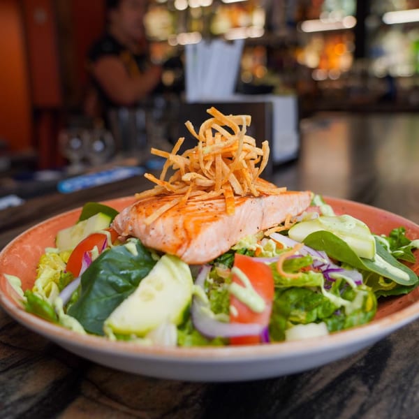 Salmon salad with mixed greens, tomatoes, cucumbers, and crispy tortilla strips at Azteca D'Oro.