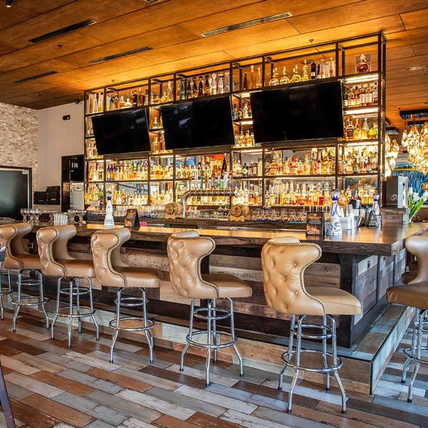 Azteca D'Oro Mexican Restaurant bar with rows of liquor bottles, three TVs, and tan leather bar stools.