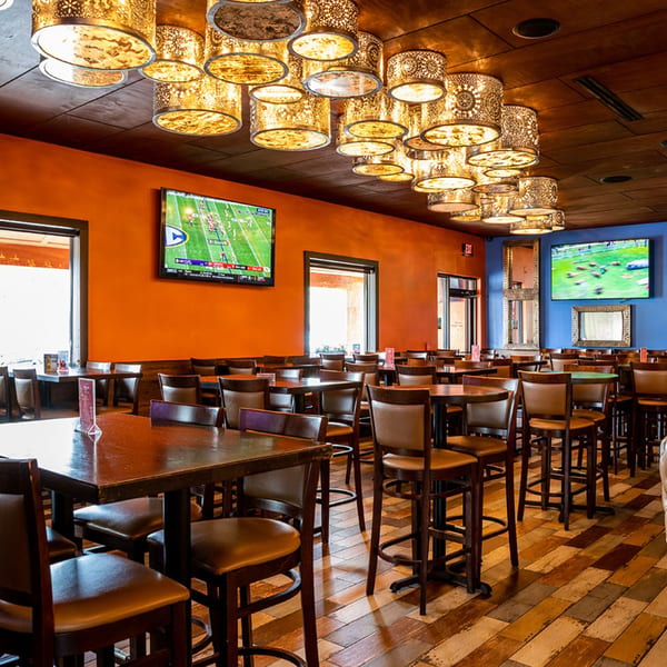 Interior of Azteca D'Oro Mexican Restaurant with tables, chairs, decorative lighting, and TVs showing sports.