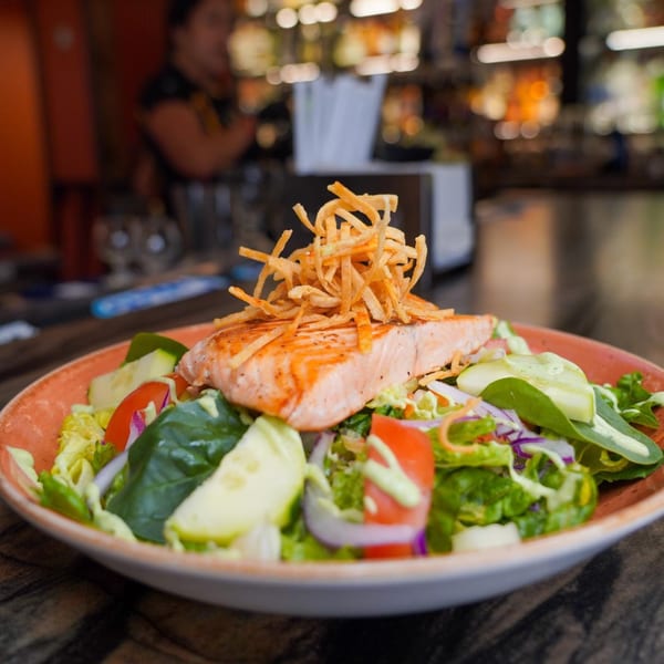Grilled salmon salad with mixed greens, tomatoes, cucumbers, and crispy tortilla strips at Azteca D'Oro.