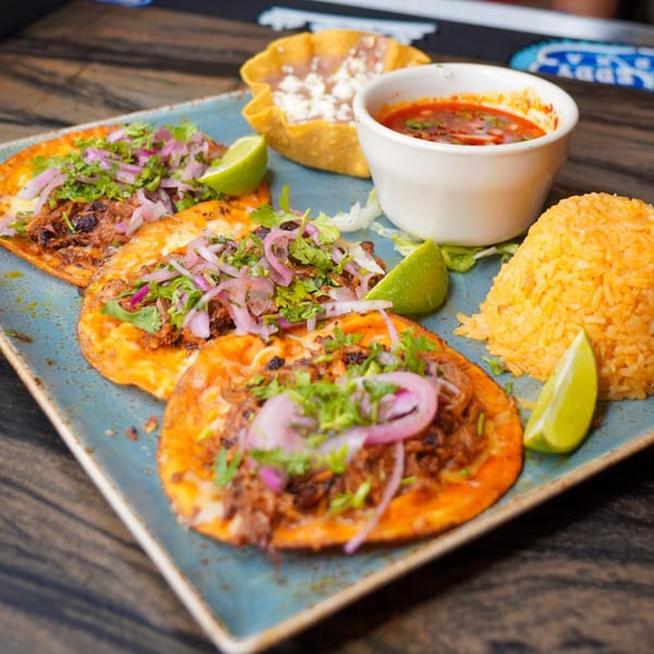 Three Azteca D'Oro Mexican birria tacos with rice, consommé, and a tostada bowl.