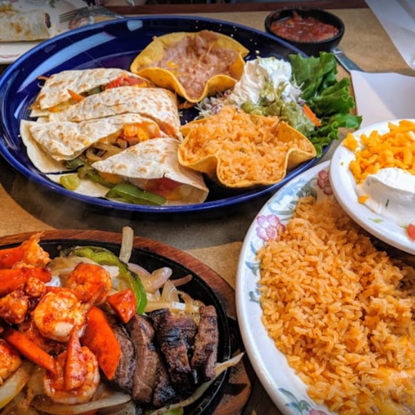 A vibrant Mexican feast with quesadillas, fajitas, rice, beans, and guacamole on a table.