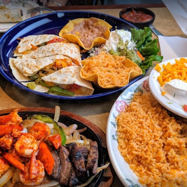 A vibrant spread of Mexican dishes, including quesadillas, fajitas, rice, and beans, on a restaurant table.