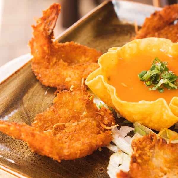 Crispy fried shrimp and a tortilla bowl filled with orange sauce and cilantro on a brown plate.