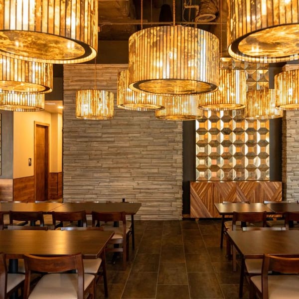 Dining room at Azteca D'Oro with warm lighting from many cylindrical pendant lamps and wooden tables.