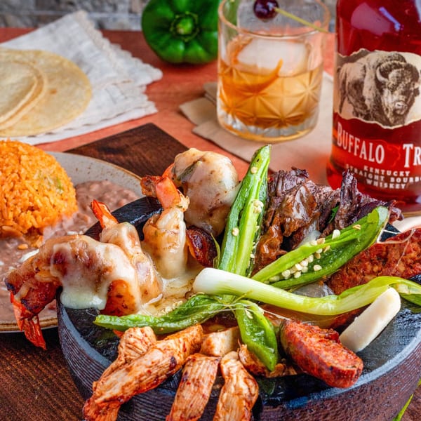 A molcajete filled with grilled shrimp, steak, chorizo, peppers, and onions, with rice and beans.