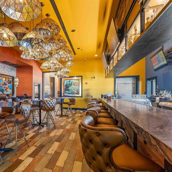 Interior of Azteca D'Oro Mexican Restaurant with a long bar, stools, and dining tables under ornate lighting.