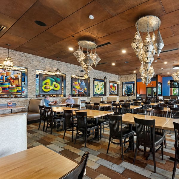 Spacious Azteca D'Oro Mexican restaurant dining room with colorful art, ornate chandeliers, and wooden tables.