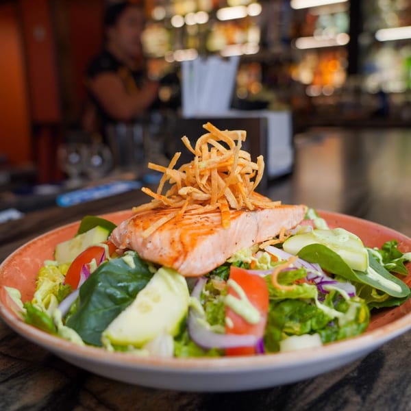 Grilled salmon salad with mixed greens, tomatoes, onions, and crispy tortilla strips at Azteca D'Oro.