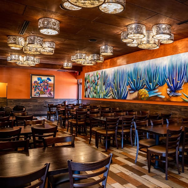 The Azteca D'Oro Mexican Restaurant dining room features vibrant murals, patterned light fixtures, and wooden tables and chairs.