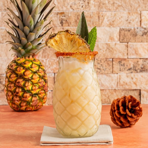 Pineapple drink in a textured glass, garnished with dried pineapple and mint, next to a whole pineapple.