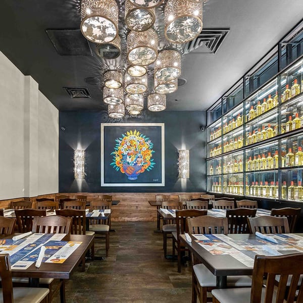 Interior of Azteca D'Oro Mexican Restaurant with tables, chairs, decorative lighting, and a wall of liquor bottles.