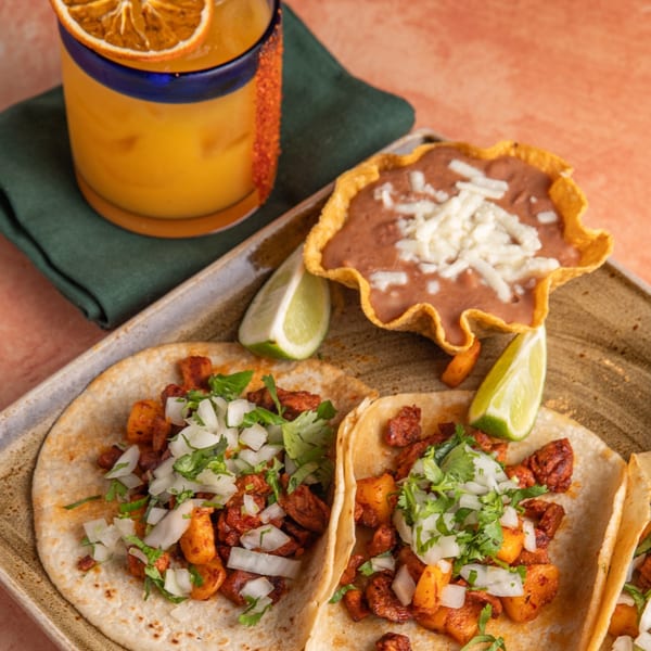 Three Azteca D'Oro Mexican tacos with a side of refried beans and a drink.