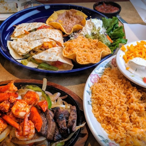 A Mexican feast with quesadillas, fajitas, rice, beans, and salsa on a wooden table.