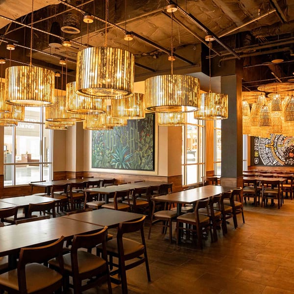 Spacious dining room at Azteca D'Oro with wooden tables, chairs, and decorative hanging lights.