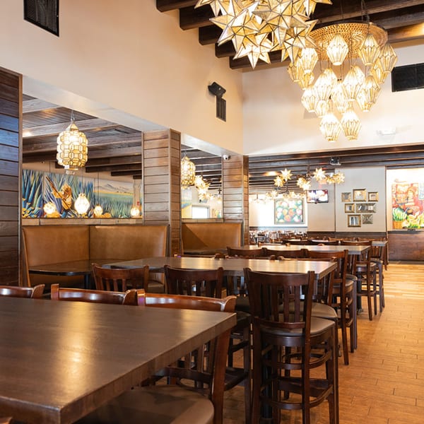 Spacious dining area at Azteca D'Oro with wooden tables, booths, and decorative Mexican star chandeliers.