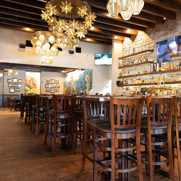Interior of Azteca D'Oro Mexican Restaurant with high-top tables, bar, and star-shaped chandeliers.