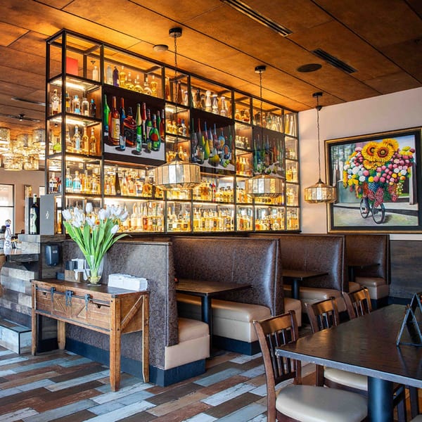Interior of Azteca D'Oro Mexican Restaurant with a large liquor display, booths, tables, and a floral painting.