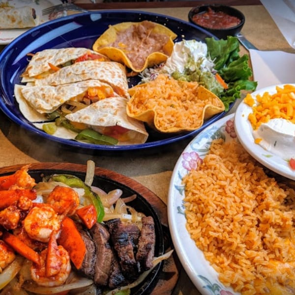 A vibrant Mexican feast with quesadillas, fajitas, rice, beans, and salsa on a table.