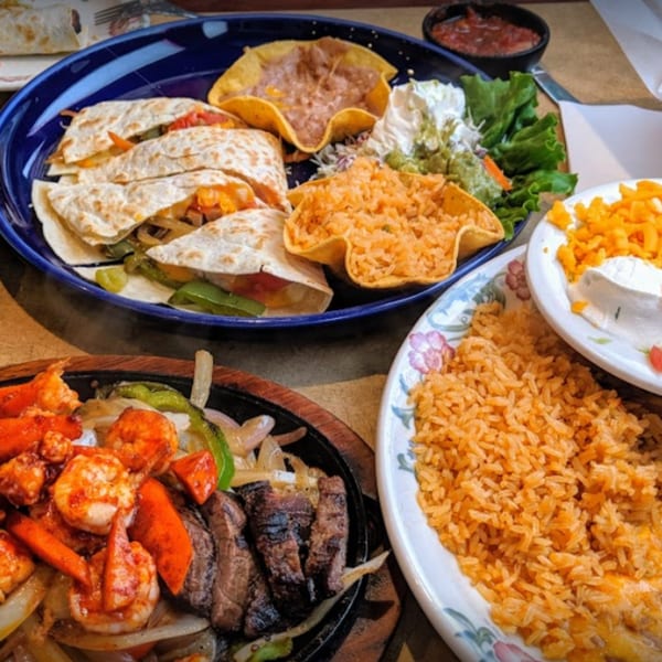 A vibrant Mexican feast with quesadillas, fajitas, rice, beans, and toppings on a table.