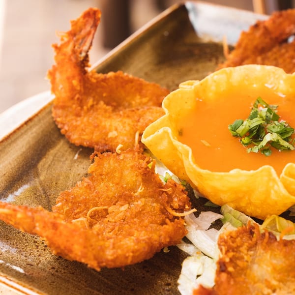 Crispy fried shrimp and a tortilla bowl filled with orange sauce and cilantro on a plate.